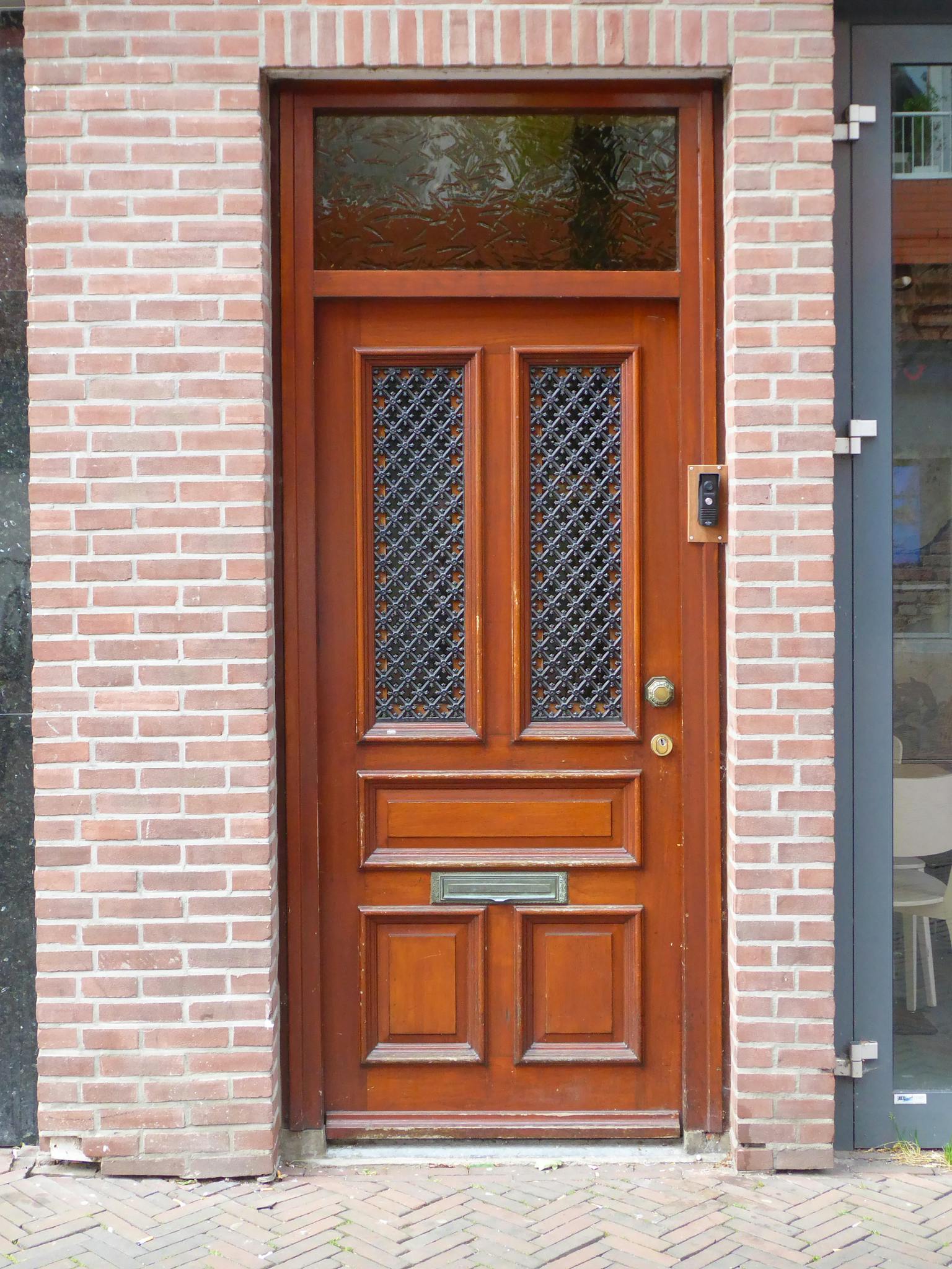 A traditional wooden door with intricate design framed by brick wall.