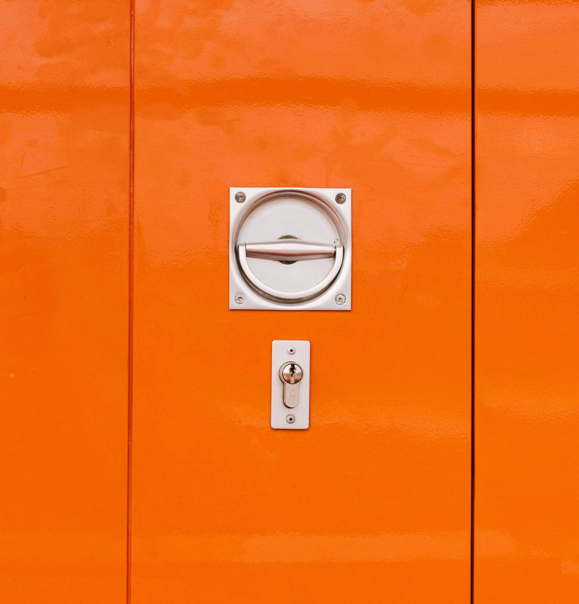 Close-up view of a vibrant orange metal door with handle and lock detail, featuring a modern minimalistic design.